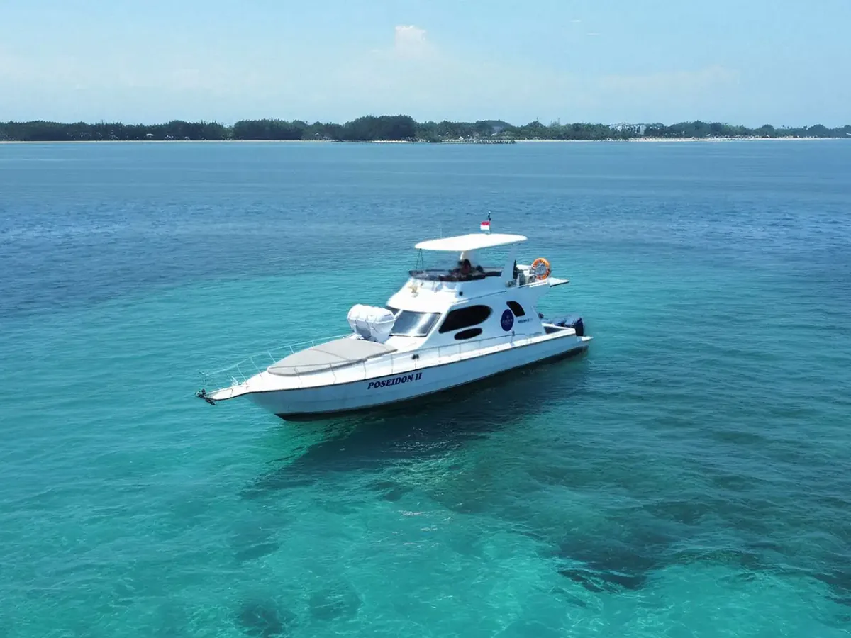 White flybridge motor yacht at anchor over turquoise shallows