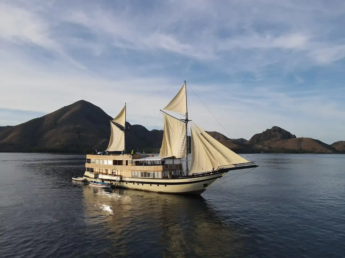 Traditional two-masted phinisi under full sail in front of dry hills in Komodo National Park